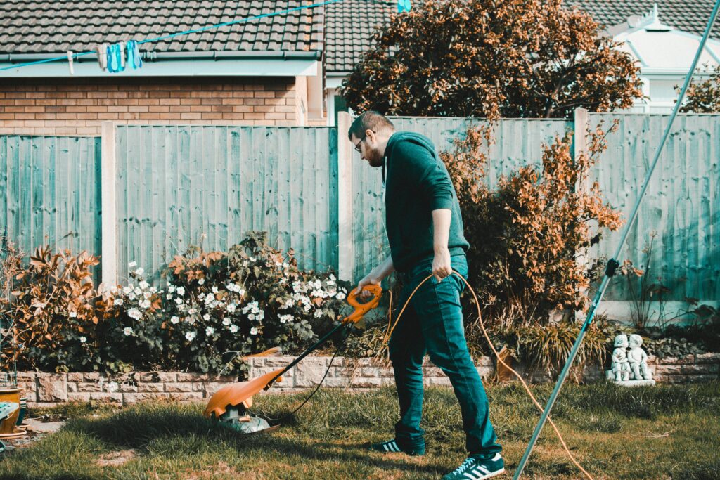 pexels-photo-1453499-1453499 A man using an electric mower in a garden on a sunny day, capturing outdoor chores and gardening vibes.